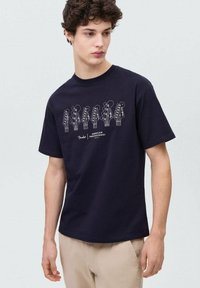 Temno modra bombažna majica z grafiko kitarskih vratu v beli barvi. Oblikovanje s krožnim ovratnikom, kratkimi rokavi in sproščenim fitom.