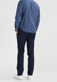 Camicetta a maniche lunghe blu navy con un piccolo motivo floreale, abbinata a pantaloni scuri e sneaker bianche, vista da dietro.