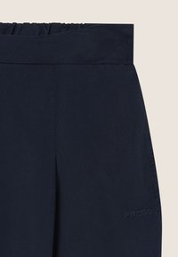 Pantalones azul marino con cintura fruncida y detalle de logo. Textura suave y diseño ajustado, aptos para uso casual o activo.