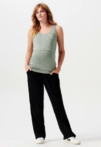 Ανοιχτό πράσινο αμάνικο τοπ με υφασμάτινο σχέδιο από πουά, συνδυασμένο με μαύρο παντελόνι φαρδύ και άσπρα αθλητικά παπούτσια.