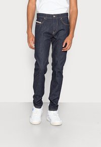 Mörkblå denim jeans med slim fit, med orange sömmar, knappstängning fram och standard femficksdesign. Matchas med vita sneakers.