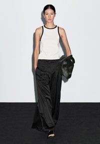 Black wide-leg pants, white tank top with black trim, and a black woven handbag. Smooth fabric, relaxed fit, minimalistic design.