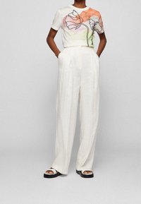 Camiseta blanca con estampado floral acuarelado en tonos rosa y verde. Pantalones blancos de tiro alto y corte holgado. Sandalias de plataforma negras.