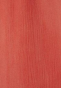 Tessuto corallo con superficie testurizzata e increspata, caratterizzato da sottili linee verticali. Il materiale sembra leggero e arioso.