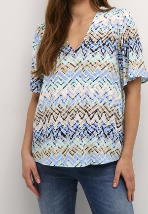 Woman wearing a short-sleeve V-neck blouse with a multicolor zigzag pattern in blue, beige, and black, paired with blue jeans.