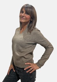 Maglione lavorato a maglia marrone chiaro con scollo a V, polsini e orlo a costine. Indossato sopra jeans scuri. Morbida texture con variazione di colore sottile.
