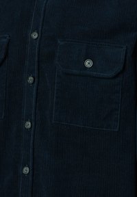 Navy Cordjacke mit zwei Brusttaschen und vorderen Knopfverschlüssen, mit vertikal geripptem Muster und metallischen Knöpfen.