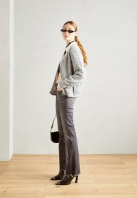 Cardigan grigio a maglia sopra un top leggero aderente, abbinato a jeans scuri a palazzo con orli sfilacciati e stivaletti neri con tacco a punta. Borsa nera e occhiali da sole.