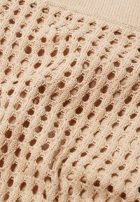 Tissu tricoté beige avec un motif ajouré composé de rangées verticales de mailles torsadées formant des trous en forme de losange.