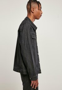 Svart denimjakke med klassisk krage, frontlukking med knapper, sidelommer og avslapet passform. Tøyet har en teksturert overflate.