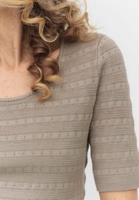 Beige neulepaita, jossa on leveä pääntie, lyhyet hihat ja teksturoituja raitoja, joissa on kohottuja pisteitä. Kangas on pehmeää ja hengittävää.