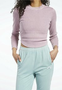 Vaaleanlila ribattu pitkähihainen crop-top, jota on yhdistetty mintunvihreisiin elastisella vyötäröllä varustettuihin jogging-housuihin, joissa on sivutaskut ja pieni logo-painatus.