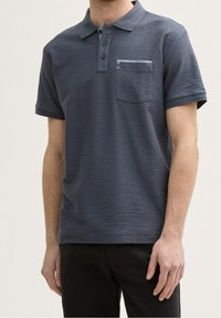 Polo à manches courtes pour homme en gris foncé, présentant une texture subtile, une patte de boutonnage à trois boutons et une poche poitrine avec des rayures horizontales.