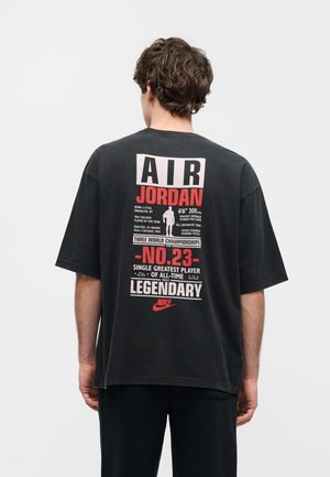 Homme de dos portant un t-shirt noir Air Jordan avec un texte rouge et blanc mettant en avant les exploits basket-ball de Michael Jordan et le logo Nike.