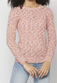 Pull tricoté en tons rouge clair et crème, avec un motif texturé, manches longues et encolure ronde. Associé à un jean bleu.