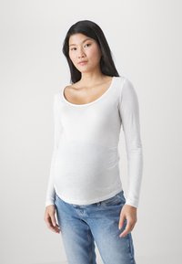 Camisa de maternidad de manga larga, blanca, en tejido ligero y suave, con escote en forma de barco, diseño ajustado y sección media extensible.