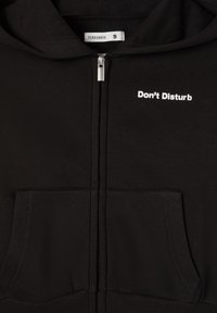 Felpa nera con zip e tasche a marsupio, con la scritta bianca "Non Disturbare" sul lato sinistro del petto e una finitura in tessuto morbido e texture.