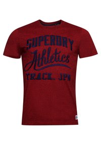 Camiseta roja de manga corta hecha de tejido texturizado, con gráficos impresos en azul "SUPERDRY Athletics TRACK. JPN" en la parte delantera.