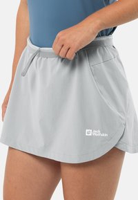 Lichtgrijze sportrok van ademend materiaal, met een tailleband met trekkoord en een zijzak. Logo zichtbaar nabij de zoom.
