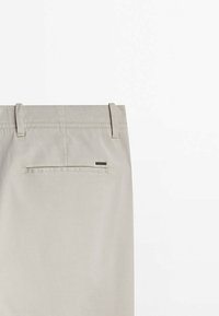 Pantalon beige clair vu de dos avec passants de ceinture et une poche passepoilée unique ornée d'une petite étiquette métallique rectangulaire de la marque.