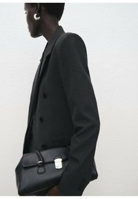 Blazer negro de doble botonadura con textura suave, combinado con un bolso de cuero negro estructurado que cuenta con un cierre de broche y un hardware minimalista.