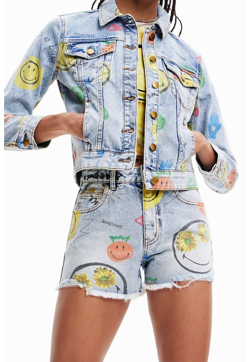 Dujakksset i denim och shorts pryds av leende ansikten och färgglada tryck på ett ljust blått tyg med fransade kanter; knappar på jackan.