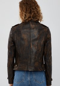 Giacca in pelle marrone invecchiata con un design aderente, spalline prominenti e una lunghezza leggermente accorciata. Presenta una texture liscia.