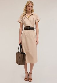 Beige shirt dress with short sleeves, button-down front, and detailed stitching. Accented with a black woven belt and a textured brown tote bag.