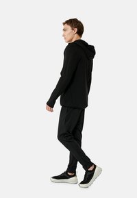 Zwarte hoodie met capuchon, slim-fit zwarte broek en zwarte sneakers met witte zolen, met een gladde textuur en minimalistisch ontwerp.