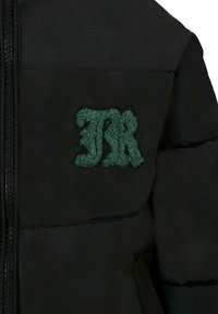 Giacca a vento nera con logo ricamato verde in peluche sul petto. Il tessuto ha una texture liscia con un design trapuntato.