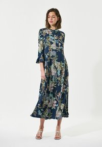 Langes marineblaues Kleid mit floralem Druck in sanften Farben. Verfügt über Dreiviertelärmel, eine fließende Silhouette und einen gerafften Saum.