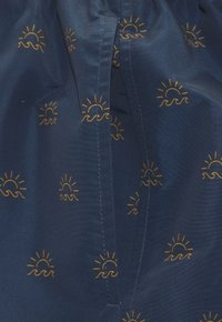 Laine navy bleu avec un motif répété de soleils dorés et de vagues. Le matériau est lisse avec un léger éclat. Détails de couture visibles.
