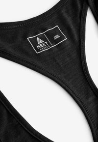 Schwarzer Sport-BH aus Aktivbekleidung mit einem V-förmigen Ausschnitt, der eine glatte Textur aufweist und ein Etikett mit der Aufschrift "NEXT ACTIVE" trägt, hergestellt in Kambodscha.