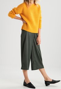Maglione giallo a maglia con un motivo testurizzato, abbinato a pantaloni cropped a gamba larga verde scuro e scarpe nere basse.