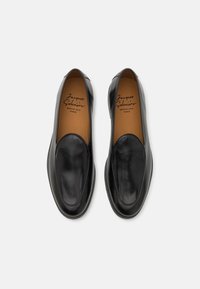 Black leather slip-on shoes with smooth texture, rounded toe, minimal stitching, and a tan leather insole featuring 'Jacques & Soloviére' branding.
