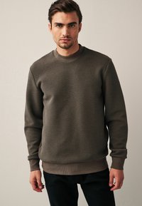 Sweatshirt marrone con texture, collo a giro, polsini e orlo a costine. Realizzato in un materiale morbido, presenta un motivo geometrico.