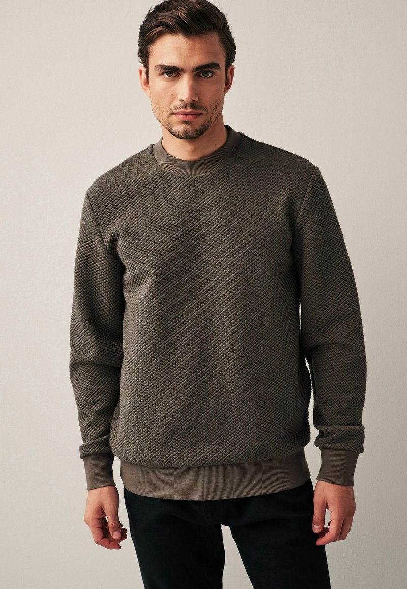 Sweatshirt marrone con texture, collo a giro, polsini e orlo a costine. Realizzato in un materiale morbido, presenta un motivo geometrico.