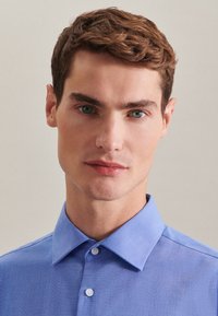 Niebieska koszula z klasycznym kołnierzykiem, gładki design i guziki z przodu. Gładka tekstura i lekki materiał.