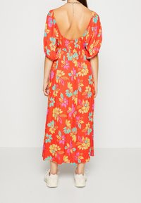 Rotes Maxikleid mit Puffärmeln und offenem Rücken, versehen mit großen, bunten Blumenmustern in Pink, Gelb und Blau. Weicher Stoff, mittellang.