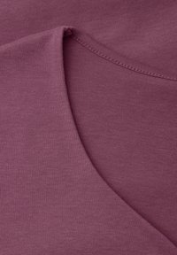 Gros plan sur un tissu violet doux présentant un col arrondi avec des coutures visibles et un détail de bord replie.