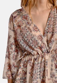 Blusa con motivo floreale in beige chiaro, con scollatura a V profonda, maniche a campana e una cintura elastica, decorata con farfalle e fiori in tonalità vivaci.