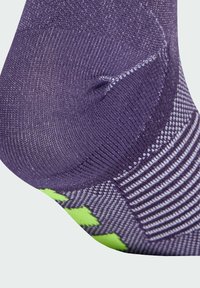 Calcetín morado con tela texturizada, puntera reforzada y acentos verdes con un patrón de rayas. El diseño es ajustado y transpirable.