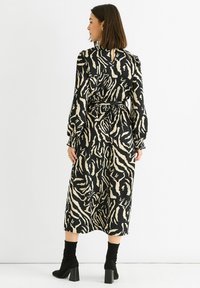 Long black and beige striped dress with long sleeves, cinched waist, and a keyhole back detail; paired with black ankle boots.