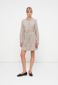 Collared shirt dress in light beige corduroy, features a belted waist, long sleeves, and button-down front. Paired with dark burgundy ballet flats.