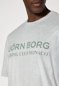 Šedé bavlnené tričko s okrúhlym výstrihom a krátkymi rukávmi, s zeleným nápisom "BJÖRN BORG TRAINING CLUB MONACO."