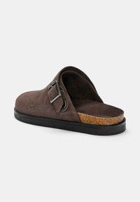 Brązowe zamszowe sandały slip-on z korkową wkładką, gumową podeszwą i metalowym akcentem w postaci klamry. Otwarte z tyłu, co ułatwia zakładanie.