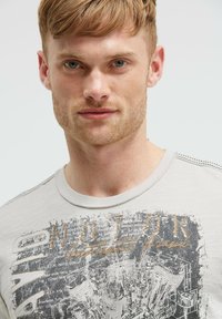 Helles graues Grafik-T-Shirt mit einem abgenutzten Druck von Motorradkomponenten und dem Text "MOTOR". Runder Halsausschnitt mit feinen Nähten.