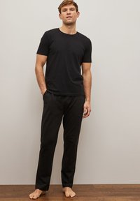 Sort crew-neck t-shirt parret med sorte bukser med elastisk talje. Begge dele er lavet af glat stof, fitted men afslappet design. Barfodet på trægulv.