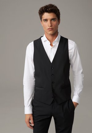 Gilet nero con chiusura a cinque bottoni, due tasche laterali e una texture liscia, indossato sopra una camicia bianca, esposto su uno sfondo neutro.