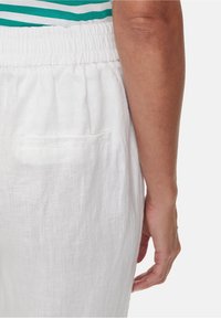 White linen pants featuring an elastic waistband and a single back pocket, showcasing a light, textured fabric.